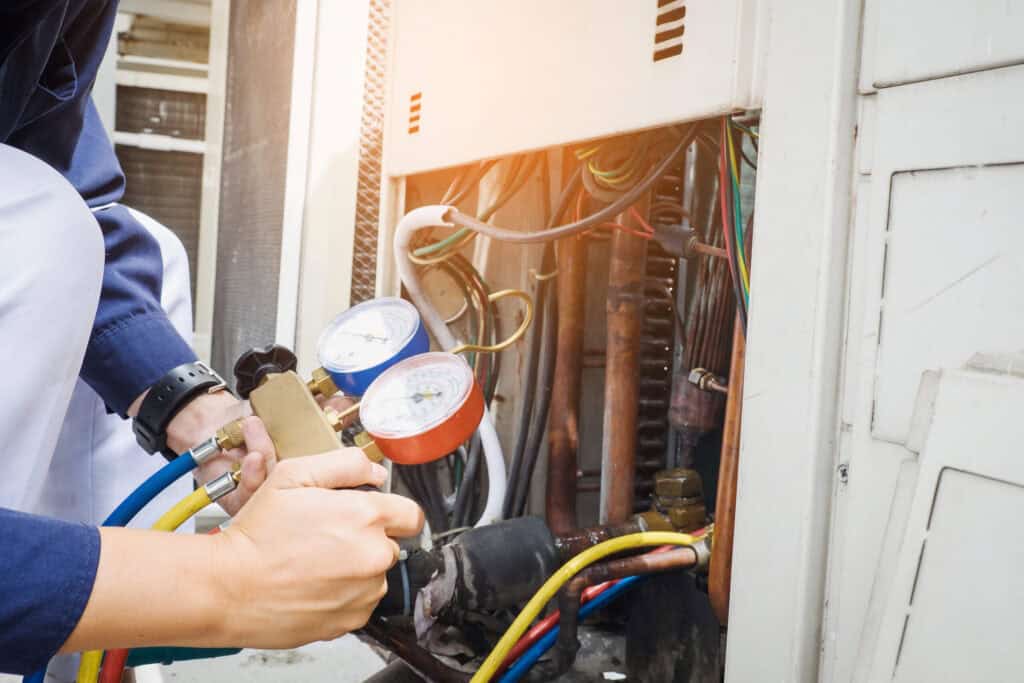 A technician expertly uses gauges to check an air conditioning unit with exposed wires and panels, highlighting the precision required in top-notch cooling services.