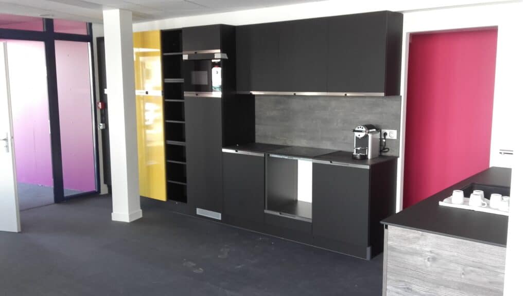 agence-lessables Intérieur d’une agence Alliance Group avec un espace chaleureux : une cuisine intégrée avec des façades noires et jaunes.