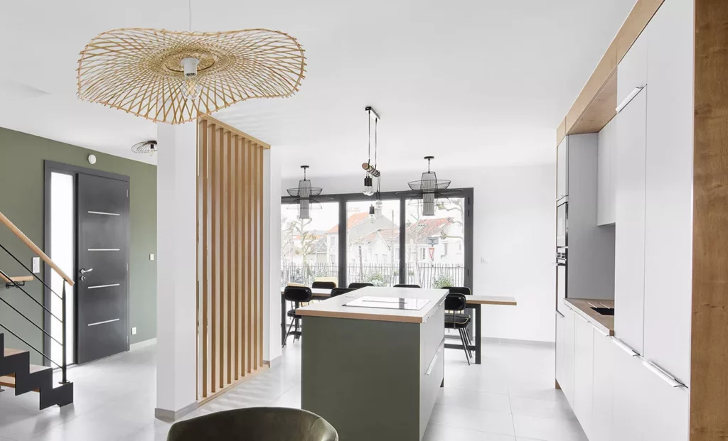 Cuisine contemporaine ouverte avec îlot central vert olive, suspensions design et cloison en bois ajourée élégante.