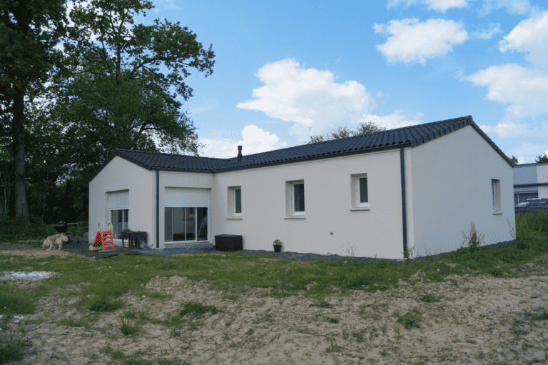 Maison de plain-pied avec toit sombre, entourée de verdure, dotée de baies vitrées et située dans un environnement naturel.