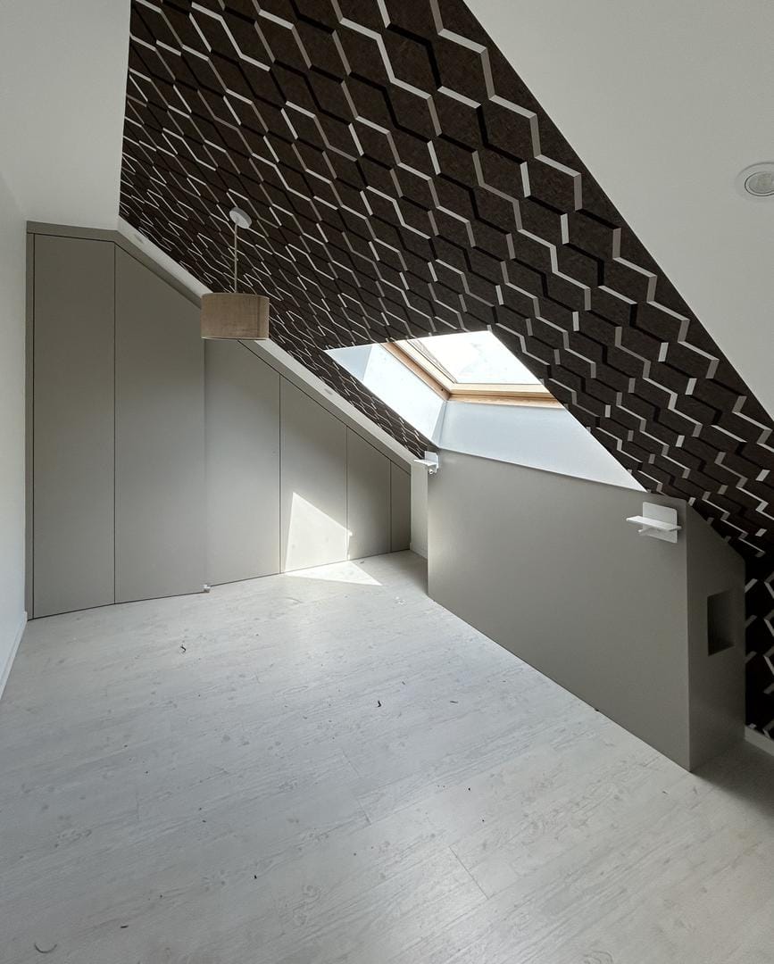 Aménagement sous combles avec des rangements intégrés et un papier peint géométrique au plafond, éclairé par une fenêtre de toit pour une ambiance lumineuse et contemporaine.