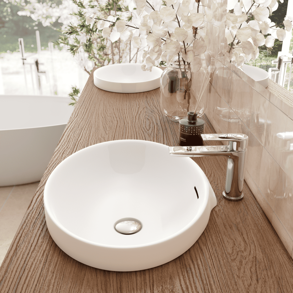Ce plan vasque en bois de chêne brun naturel met en valeur des vasques rondes en céramique blanche pour un look intemporel et épuré. L’association du bois et de la robinetterie chromée apporte un équilibre parfait entre la chaleur du naturel et la modernité du design. Les détails comme les carreaux muraux en beige et la lumière extérieure qui illumine l’espace soulignent une atmosphère douce et relaxante, idéale pour une salle de bain apaisante et fonctionnelle.
