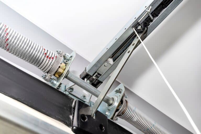 Close-up of a garage door mechanism, revealing the metal springs, cables, and tracks. The intricate components prompt questions about the engineering behind the smooth opening and closing process.