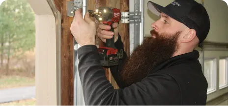 Man uses a power drill to install or repair a garage door track in a garage setting.