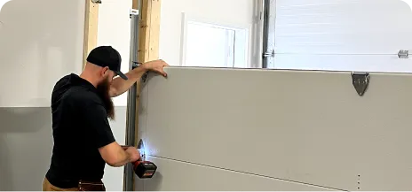 Person wearing a cap and using a power drill to install a garage door panel.
