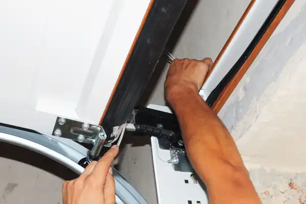 A person expertly adjusting a garage door mechanism with both hands, focusing on the tension cables, hinges, and roller repair for seamless operation.