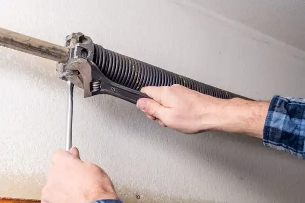 A person skillfully adjusts a garage door spring with a wrench and screwdriver, ensuring smooth operation.
