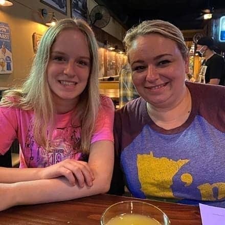 Two people, deep in conversation about their office careers, sit at a wooden table in a dimly lit restaurant adorned with framed pictures. A glass filled with yellow liquid rests between them, adding a touch of color to the intimate setting.