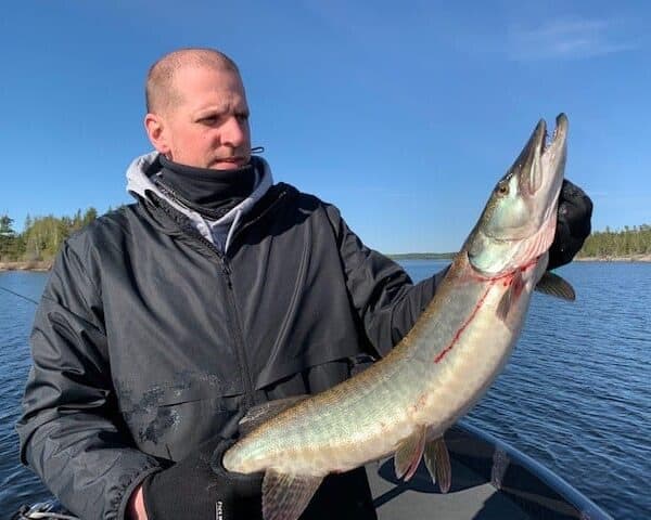 A Plumbing Service Technician proudly holds a large fish on a boat in the lake, basking under the clear blue sky.