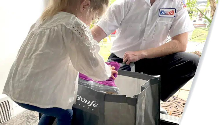 A child carefully places pink shoes into a shopping bag held by someone in a white shirt with a logo, reflecting the warm spirit of community in Minnesota.