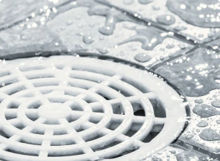 Close-up of a round, white shower drain with water droplets on a textured tile surface.