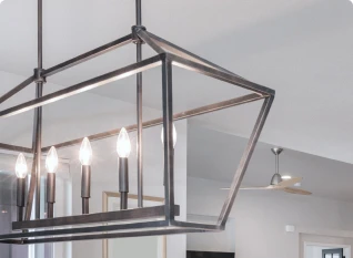 Rectangular metal chandelier with five exposed light bulbs, hanging from the ceiling in a modern room with a fan in the background.
