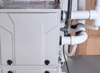 Close-up view of a modern HVAC unit with visible pipes and connectors, installed indoors against a wooden door.