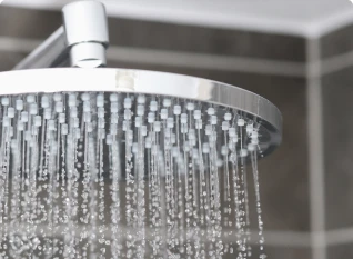 Close-up of a silver showerhead with water streaming down in a tiled bathroom.