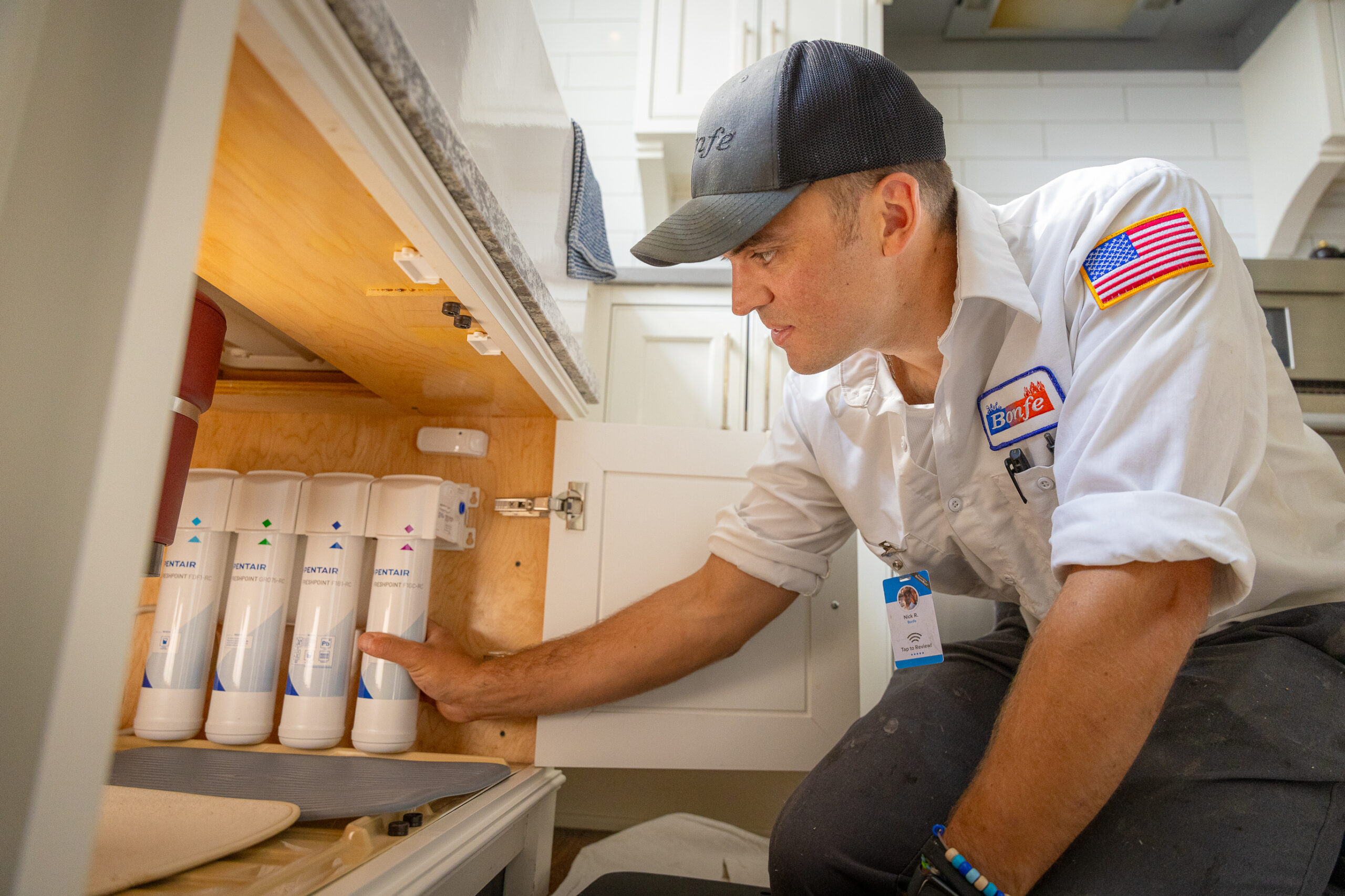 A technician in uniform installs or inspects a multi-stage Reverse Osmosis Systems water filtration unit under a kitchen sink.