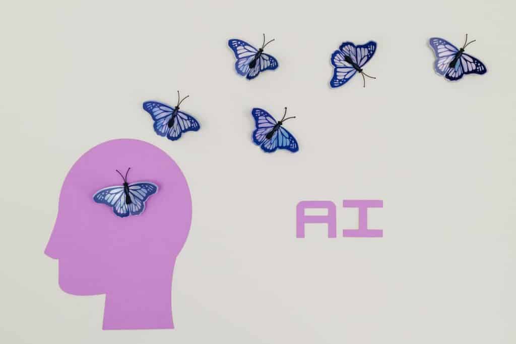 An image of a purple human head, with butterflies flying out of the head and the word "AI" in purple. This image represents upskilling yourself in AI, which is important when considering how to get into AI.