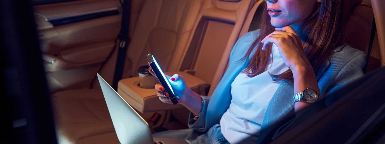 Woman using mobile phone and laptop in car