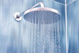 Close-up of a round, silver showerhead with water streaming down in a blue-tiled shower, offering endless hot water and energy savings for St. Paul & Minneapolis homes.