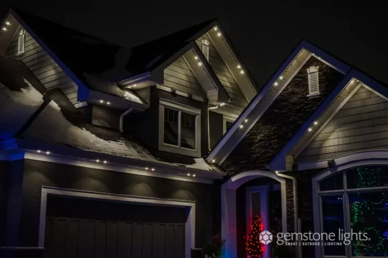 A house at night with snow on the roof, illuminated by white LED outdoor lights along the eaves and gables.