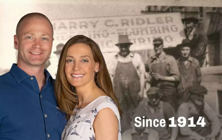 A man and woman smile in front of a faded, vintage photo of workers, with the text "Since 1914" displayed in the lower right corner.