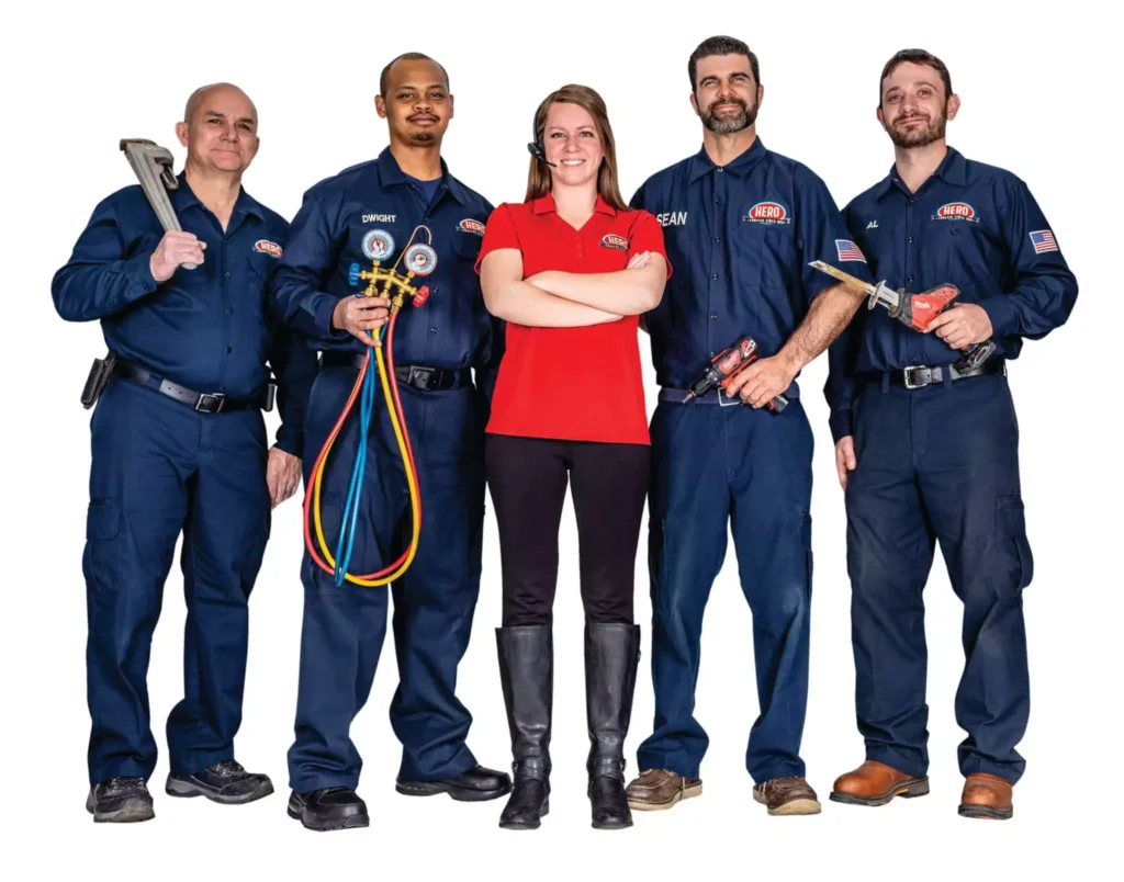 Five people pose for a group photo; four wear navy work uniforms holding tools, and one in a red shirt stands in the center with arms crossed, all facing the camera.