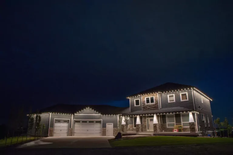 A two-story house with a three-car garage is illuminated by string lights along the roofline at night.