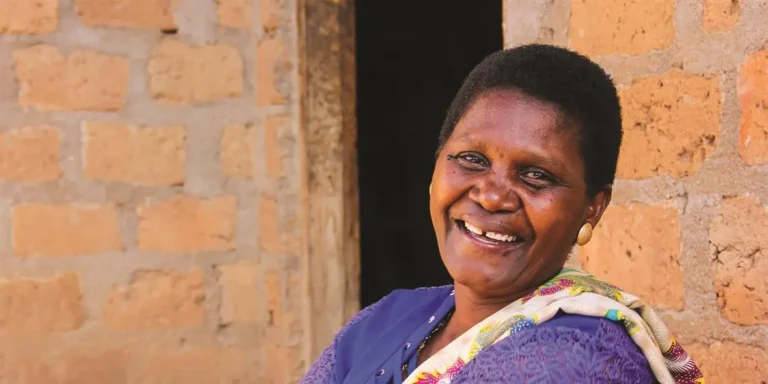 A woman smiles in front of a brick wall, wearing a purple top and a patterned cloth draped over her shoulder—a true hero giving back to the Twin Cities community.