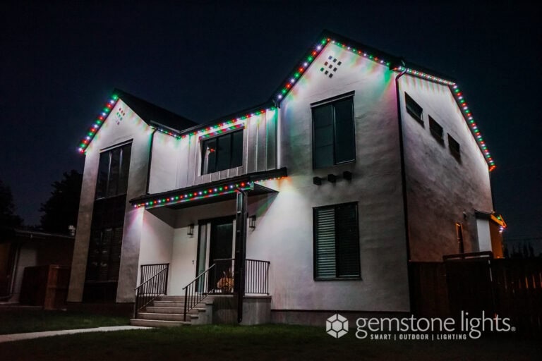 A modern two-story house at night with multicolored LED lights outlining the roofline and eaves.