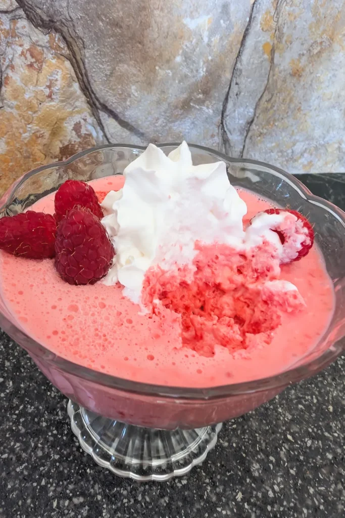 looking down on an angle at the top of the no-bake raspberry cream cheese salad in a dessert cup topped with whipped cream and berries