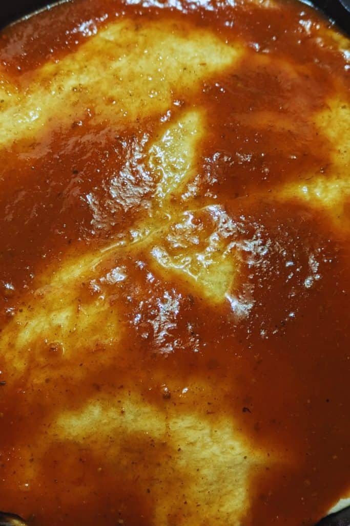 red enchilada sauce spread on top of taco bake