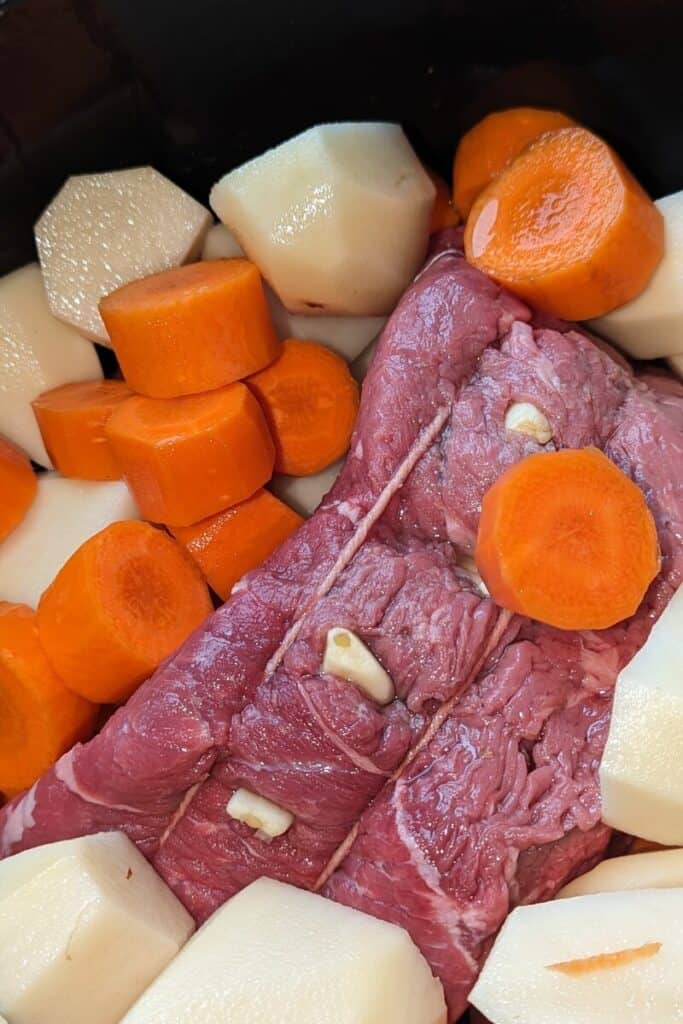 adding potatoes and carrots around roast beef