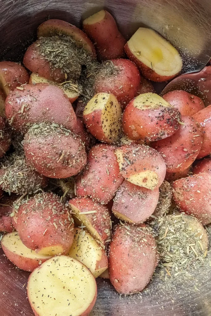 adding Italian herbs and pepper to potatoes in bowl