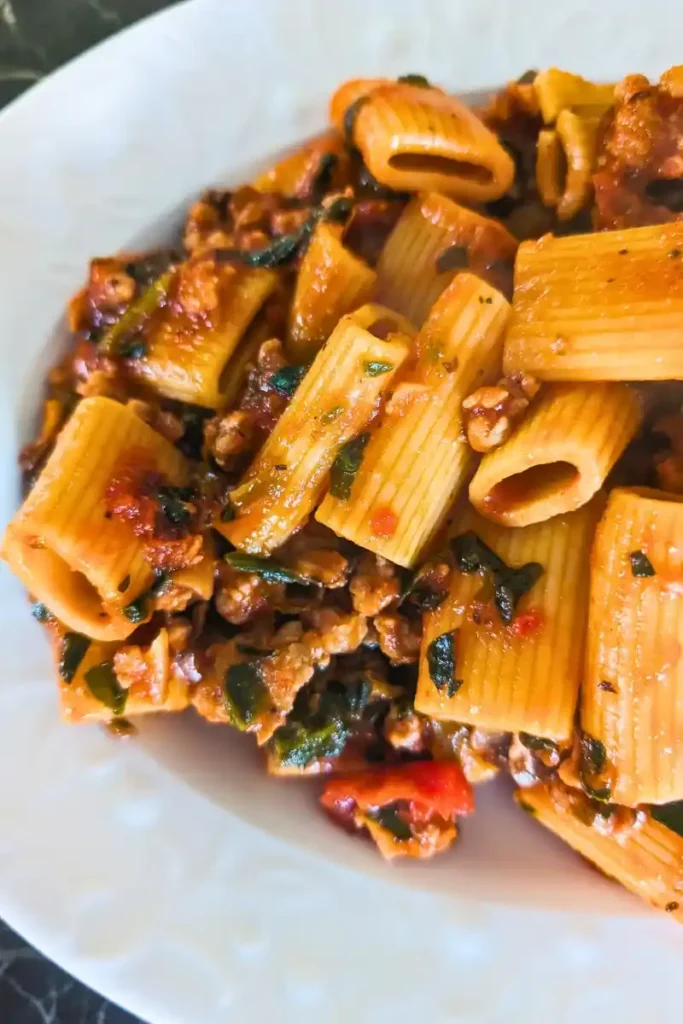 the tomato basil rigatoni with crumbled sausage and mushroom sauce on an oval white plates as seen from above one end