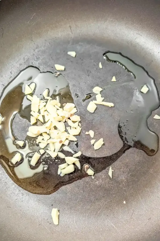 slivered garlic cloves in frying pan with olive oil
