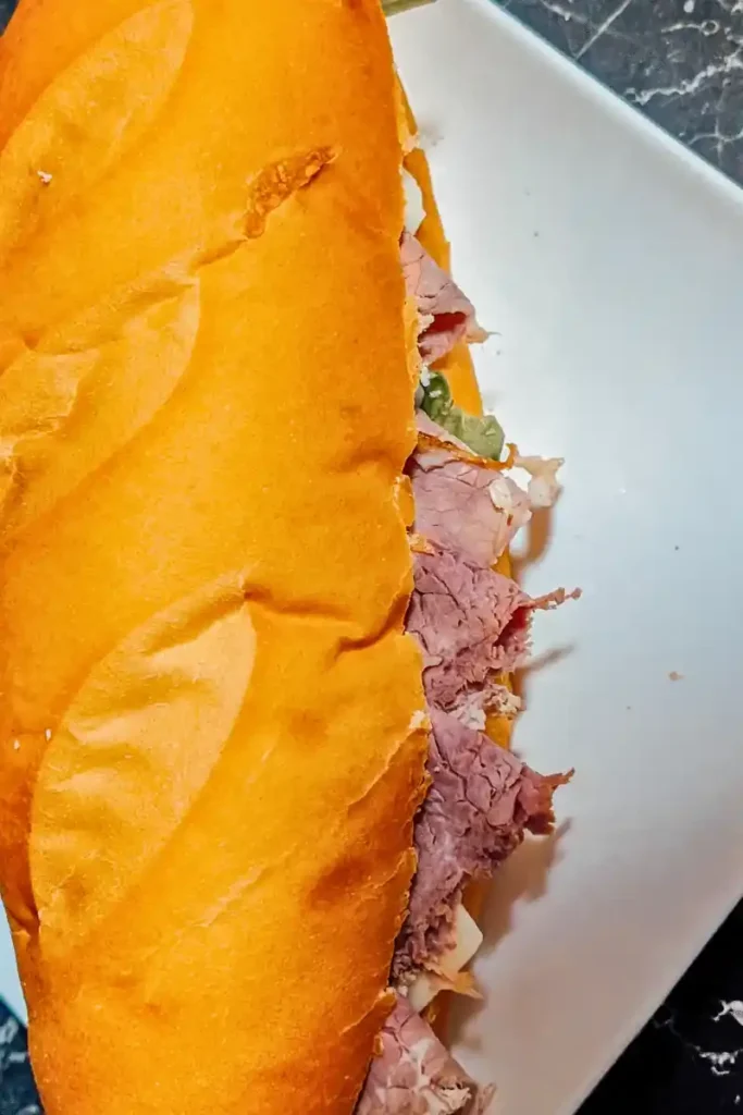 the edge of the roast beef sub sitting on white plate meat portruding from cut edge