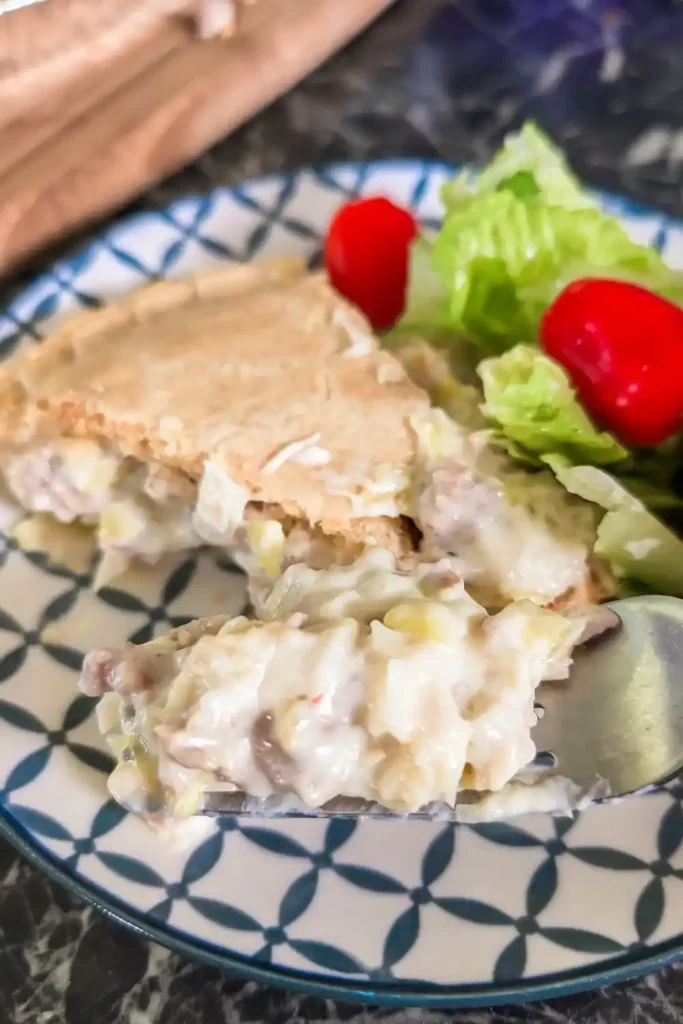 a slice of meat pie on fork with side salad and blue and white plate