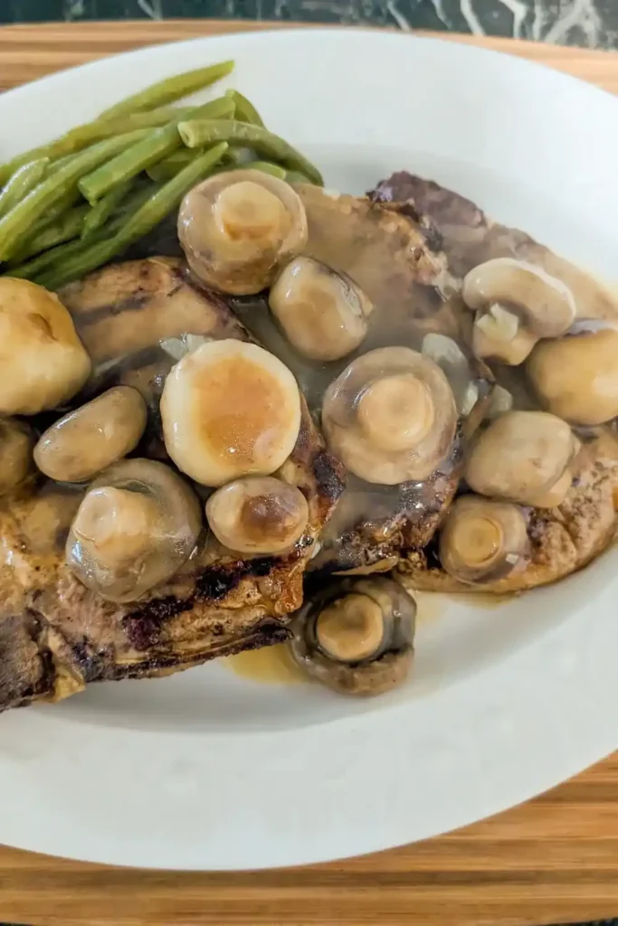 golden button mushroom sauce over grilled pork chops steamed green beans on white plate