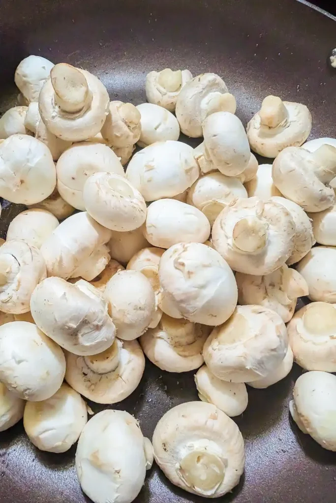 white button mushrooms in hot frying pan with olive oil