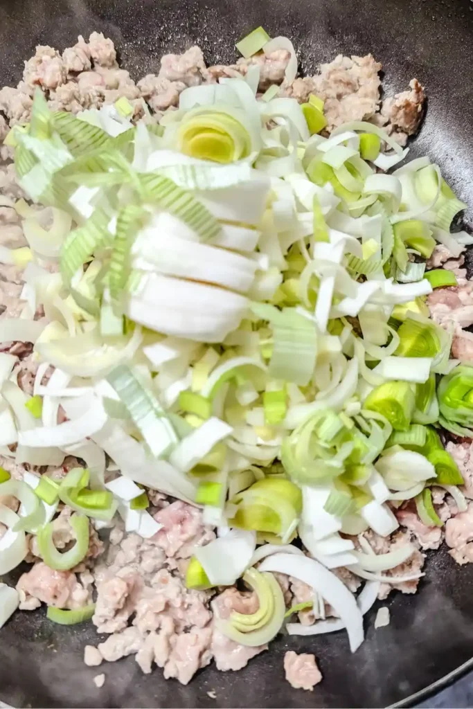 adding leeks to crumbled sausage in fry pan