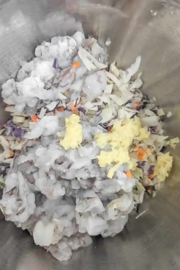 adding fresh grated ginger to raw shrimp and coleslaw mix in stainless steel bowl