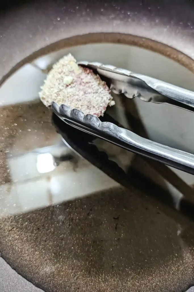 placing with tongs pork panko coated medallion in hot oil