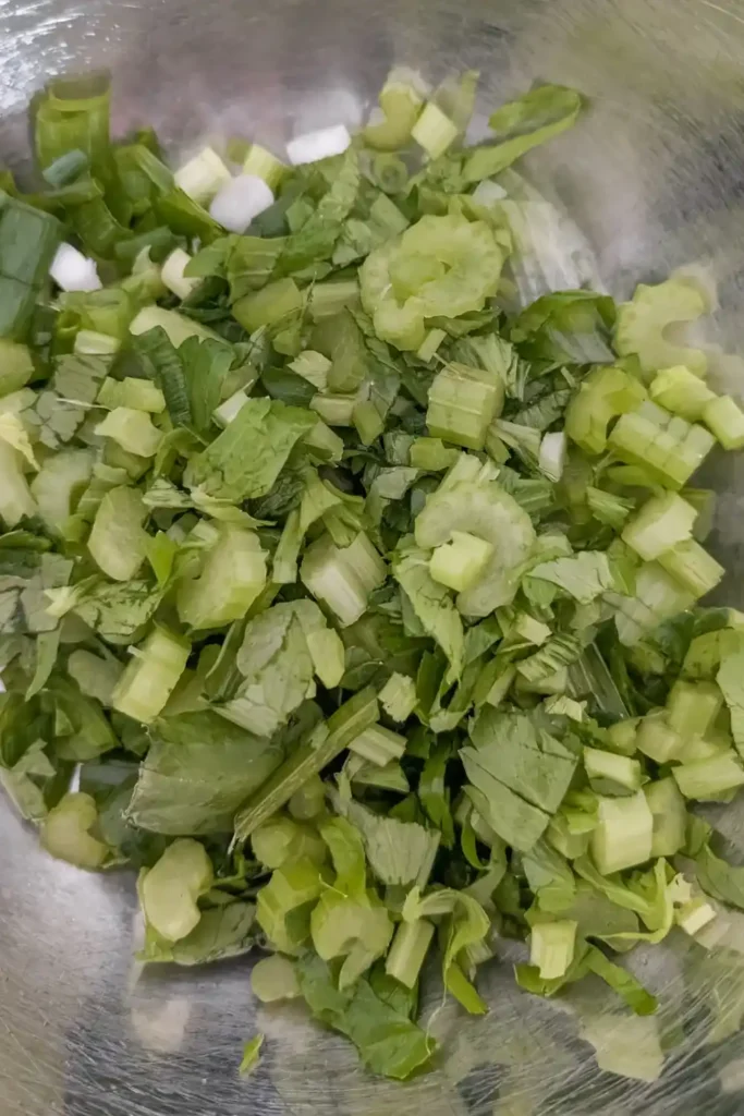 cut up celery, celery leaves, green onion in stainless steel bowl