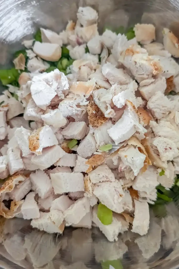 cut up white chicken meat in stainless steel salad bowl with celery and green onion