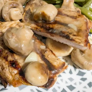 recipe card image of golden button mushroom sauce over cut grilled pork chop