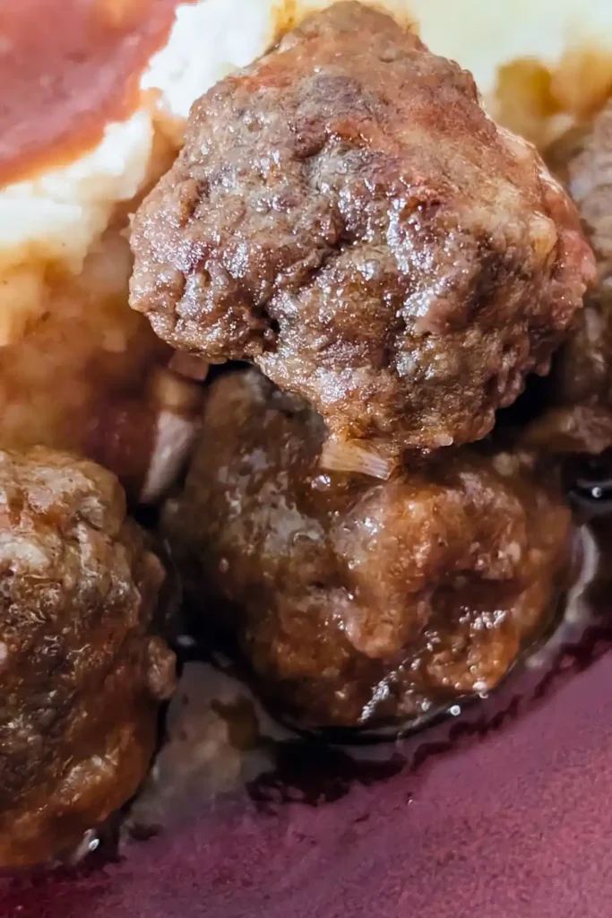 three bbq meatballs beside some mashed potatoes with sauce in back left corner