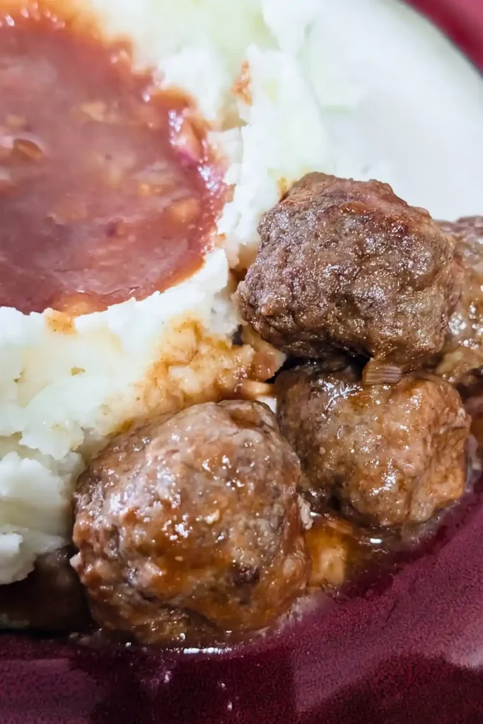 three meatballs on red trimmed plate with mashed potatoes with a well in center filled with extra bbq sauce