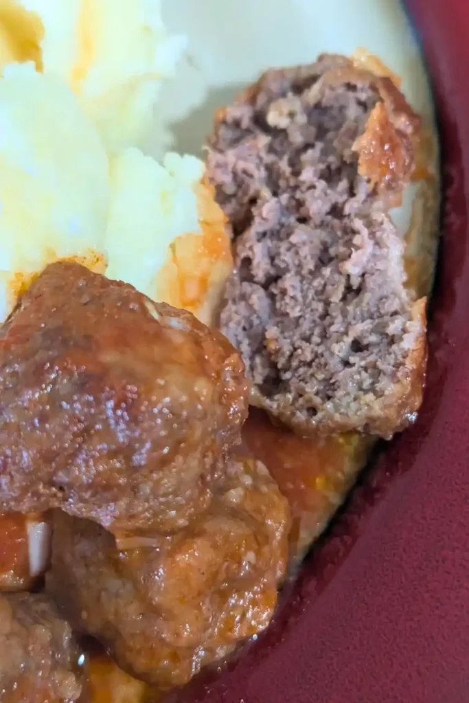 the saucy meatballs on the side of a plate one is cut in half revealing its cooked center
