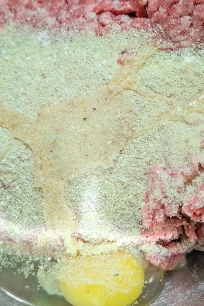 adding bread crumbs and egg to lean ground beef for meatball mixture
