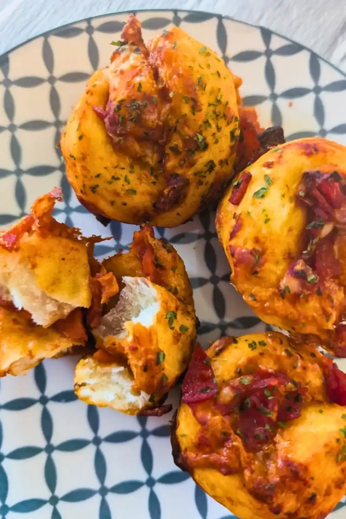tearing apart a mini pizza muffin on a blue and white patterned plate with three other mini pizza muffins