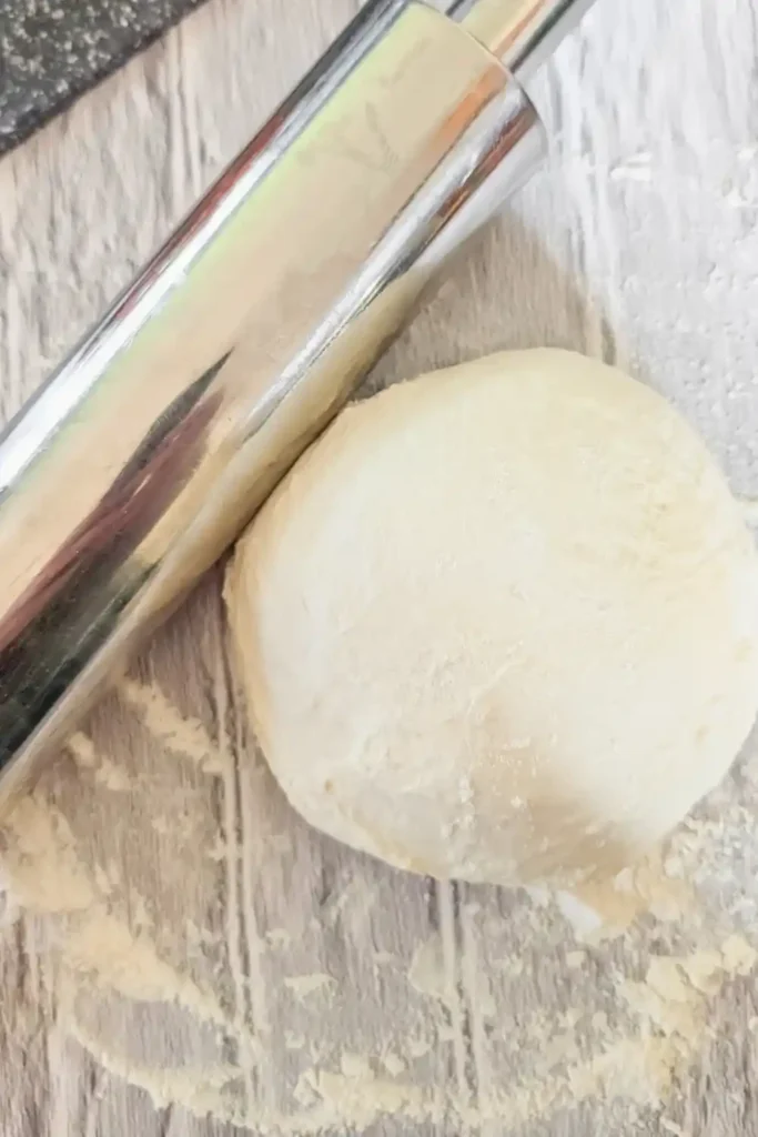 pizza dough ball with stainless steel rolling pin on lightly floured surface